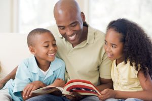 Smiling father with his two happy children looking at a magazine.