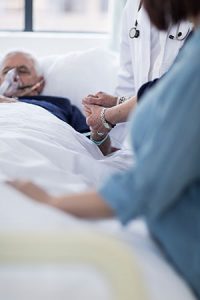 Sick older man in a hospital bed with a family member.